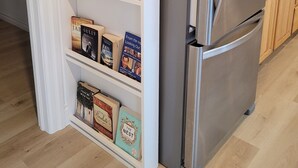 A modern kitchen with a stainless steel refrigerator, wooden cabinets, and a built-in bookshelf with various books.