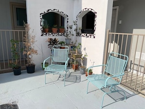 Un balcon avec deux chaises en métal, des plantes en pot et une petite table.