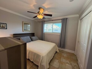 A bedroom with a bed, a ceiling fan, a window with curtains, a door, and a framed picture on the wall.