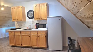 A kitchen with wooden cabinets, a microwave, a refrigerator, and a clock on the wall.