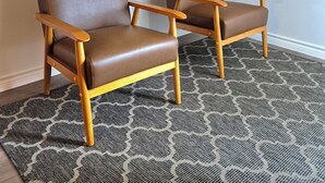 Two brown leather chairs with wooden armrests and legs, placed on a patterned rug in a room with a sloped ceiling and a framed picture on the wall.