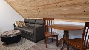 A cozy room with a dark leather sofa, a patterned ottoman, and a wooden dining table with chairs.