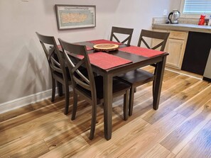 Un coin repas avec une table et des chaises en bois, des sets de table rouges et une carte encadrée accrochée au mur.