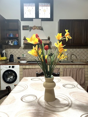 Una cocina con una mesa, una lavadora y un jarrón con flores.