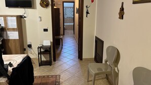 A living room with a TV, a desk with a computer, a chair, a sofa, and a hallway leading to a bathroom.