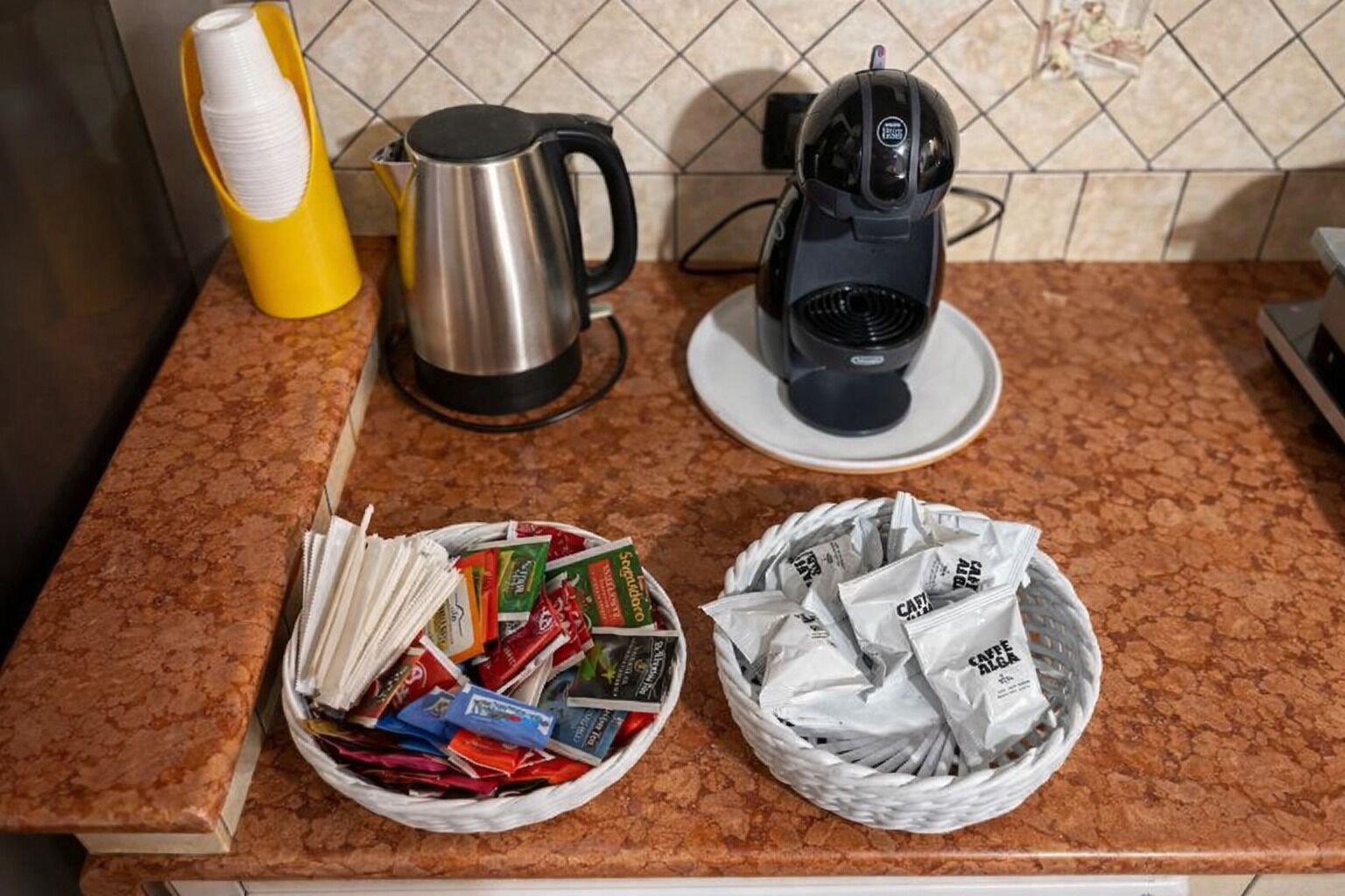 Een keukentrap met een koffiezetapparaat, een waterkoker en twee manden met koffiekapsules en -hoeveelheden.