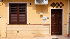 A building facade with a brown door, a window with brown shutters, and an air conditioning unit mounted on the wall.