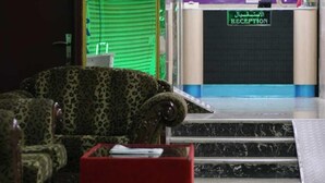 A reception area with a reception desk, a green-striped window, and a sign indicating a luggage store.