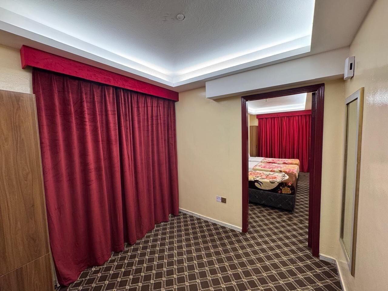 A hotel room with a checkered floor, a bed with a floral bedspread, and red curtains.