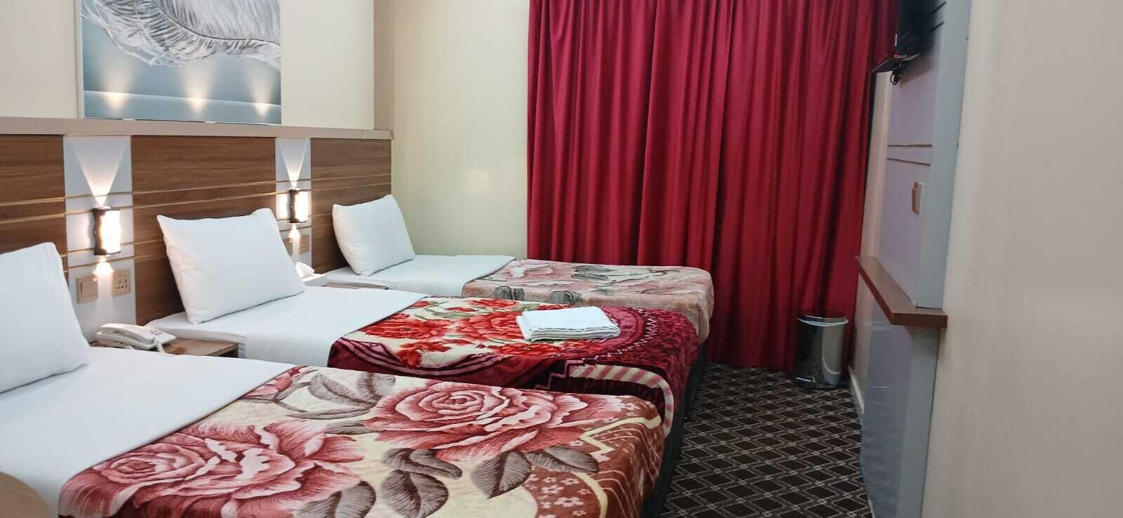 A hotel room with two beds, a red curtain, a wall-mounted lamp, and a small trash bin.