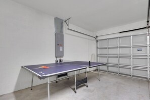 Une table de ping-pong dans un garage, avec une étagère en métal et une prise de courant.