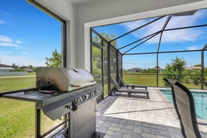 A patio area with a grill, outdoor seating, and a view of a swimming pool.