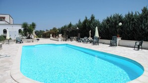Une piscine entourée d’un patio carrelé et de verdure, avec des chaises longues et des parasols.