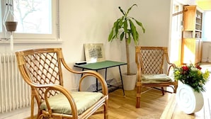 Ein Zimmer mit zwei Korbstühlen, einem kleinen Tisch, einer Topfpflanze und einer Holzkiste.