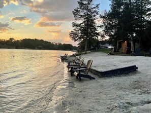 A lakeside setting with wooden chairs and a small wooden structure, likely a cabin or shed, near the water's edge.