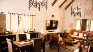 A cozy living room with a wooden dining table, comfortable seating, a flat-screen TV, and a sofa with a patterned throw. - 3 Bedroom House Sleeps 6, Mini Bar, Free Parking (Livingstone)