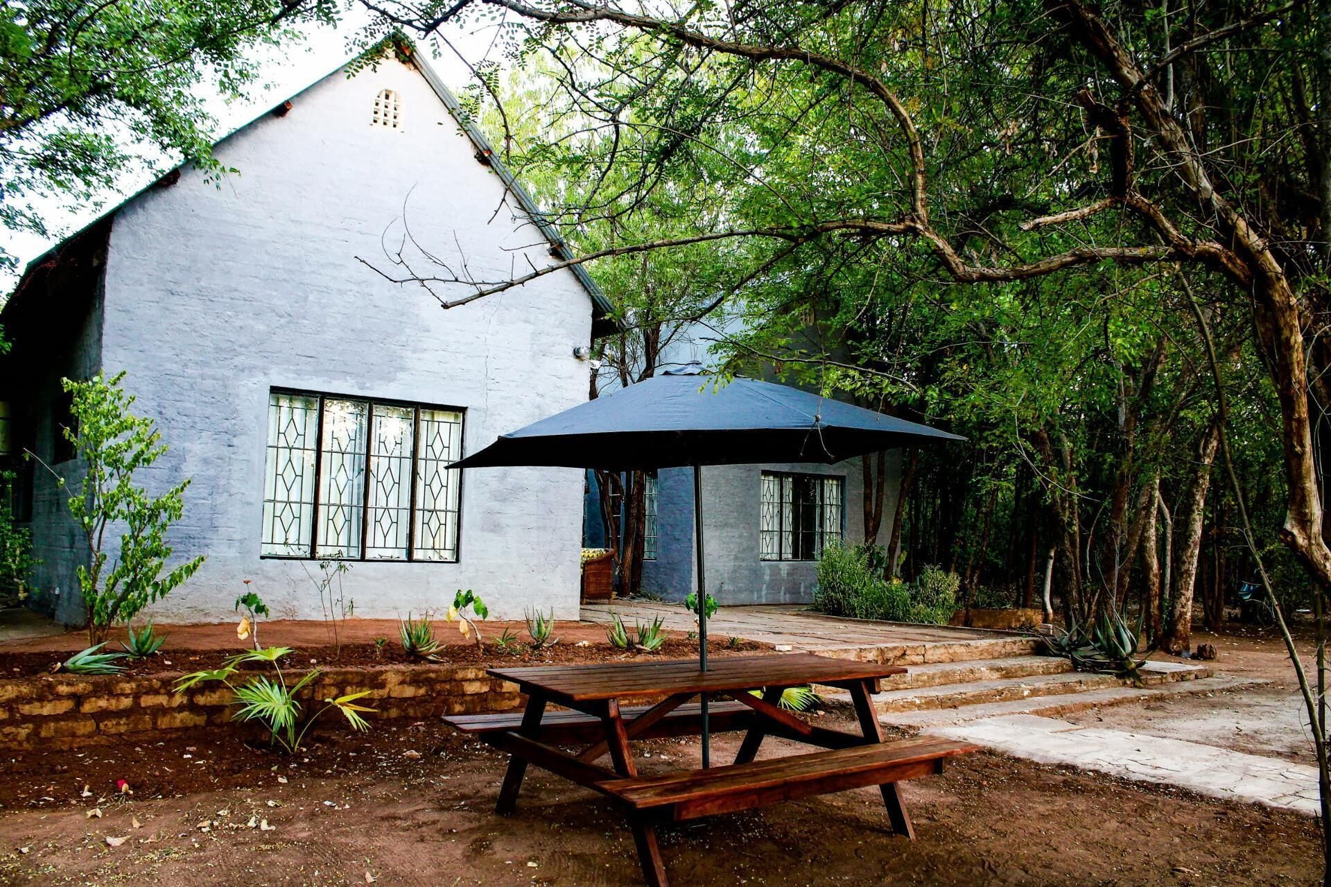 Una casa rústica de paredes blancas, una mesa de picnic de madera y un paraguas grande.