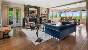 A spacious living room with a stone fireplace, a blue sofa, and a dining area with a view. - Saratoga's Musical Oasis|Heated Pool|King Bed|Mountain Views| (Greenfield center)