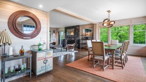 A spacious living room with a fireplace, dining area, and a large window offering a view of greenery. - Saratoga's Musical Oasis|Heated Pool|King Bed|Mountain Views| (Greenfield center)