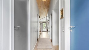 Um corredor com teto de madeira, porta azul e vista para um quarto com mesa e cadeiras.