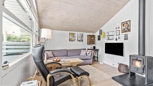Uma sala de estar aconchegante com sofá, cadeiras, mesa, televisão e lareira a lenha.