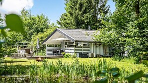 Uma cabana com varanda, rodeada por vegetação exuberante e um lago.