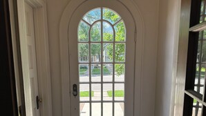 A white arched door with a grid of glass panes, leading to an outdoor view with greenery and a building in the distance. - Large Waterfront Lake Michigan - Book Fall Colors! (Menominee)