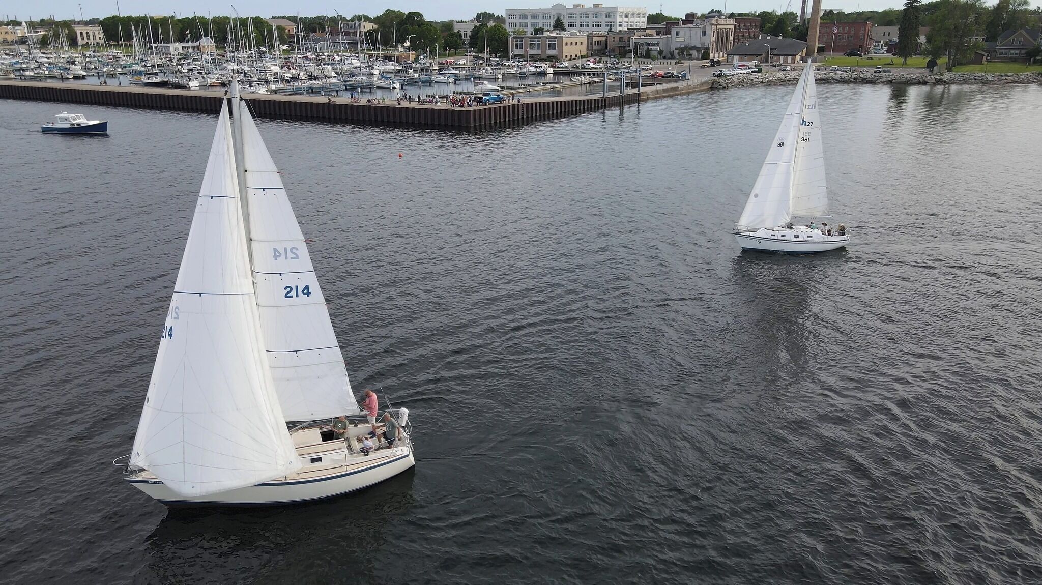 Deux voiliers sur une étendue d’eau calme, avec une marina en arrière-plan.