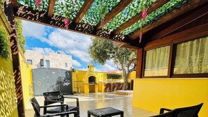 An outdoor patio with black metal chairs and tables, a yellow wall, and a view of the cityscape.
