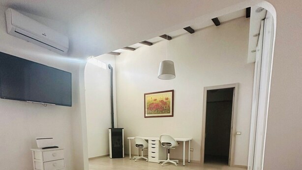 A modern living room with a white table, a TV mounted on the wall, a painting on the wall, and a door leading to another room.