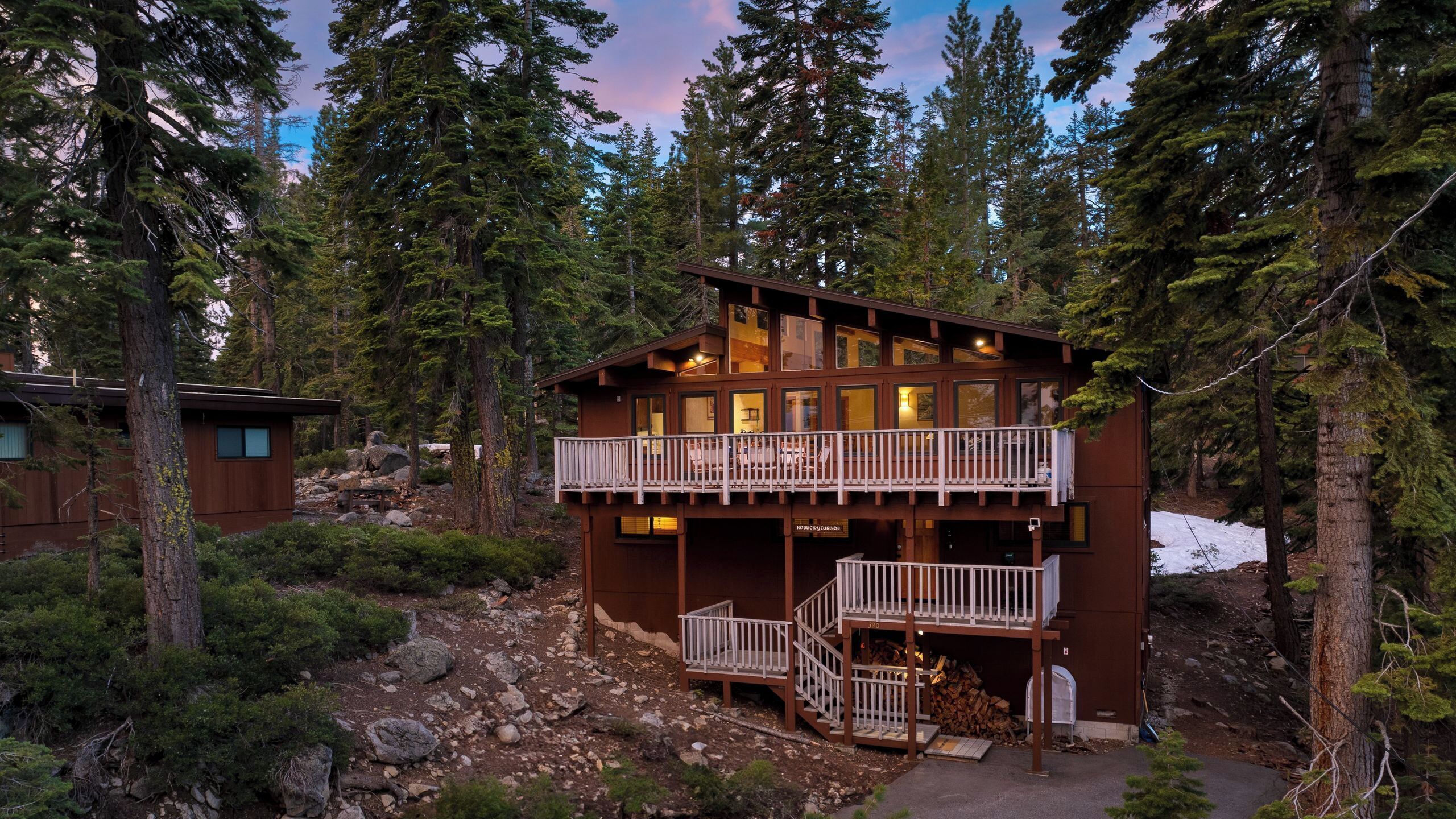 A two-story cabin with a balcony, surrounded by trees.