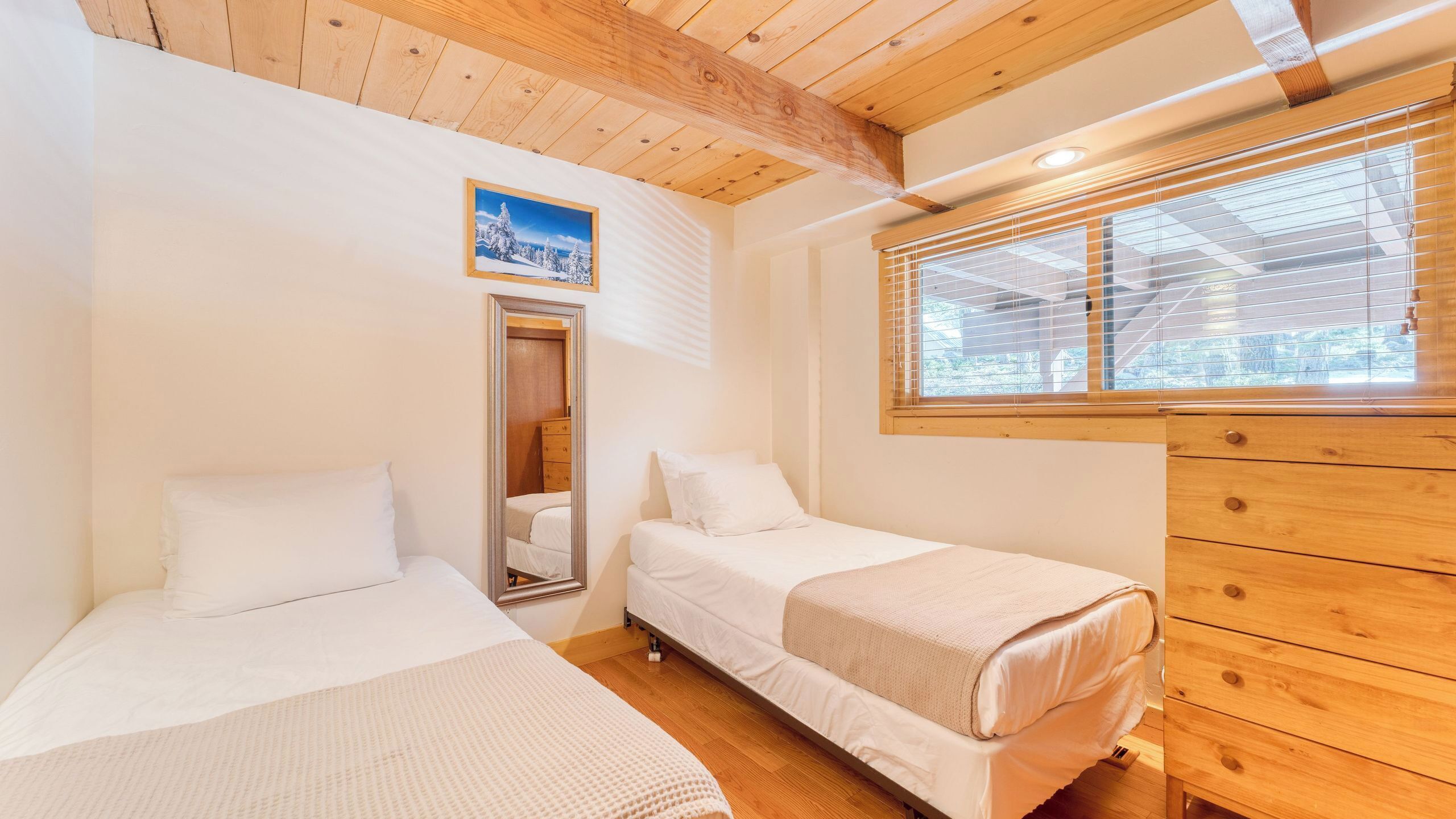 A bedroom with two beds, wooden ceiling beams, a window with blinds, and a dresser.