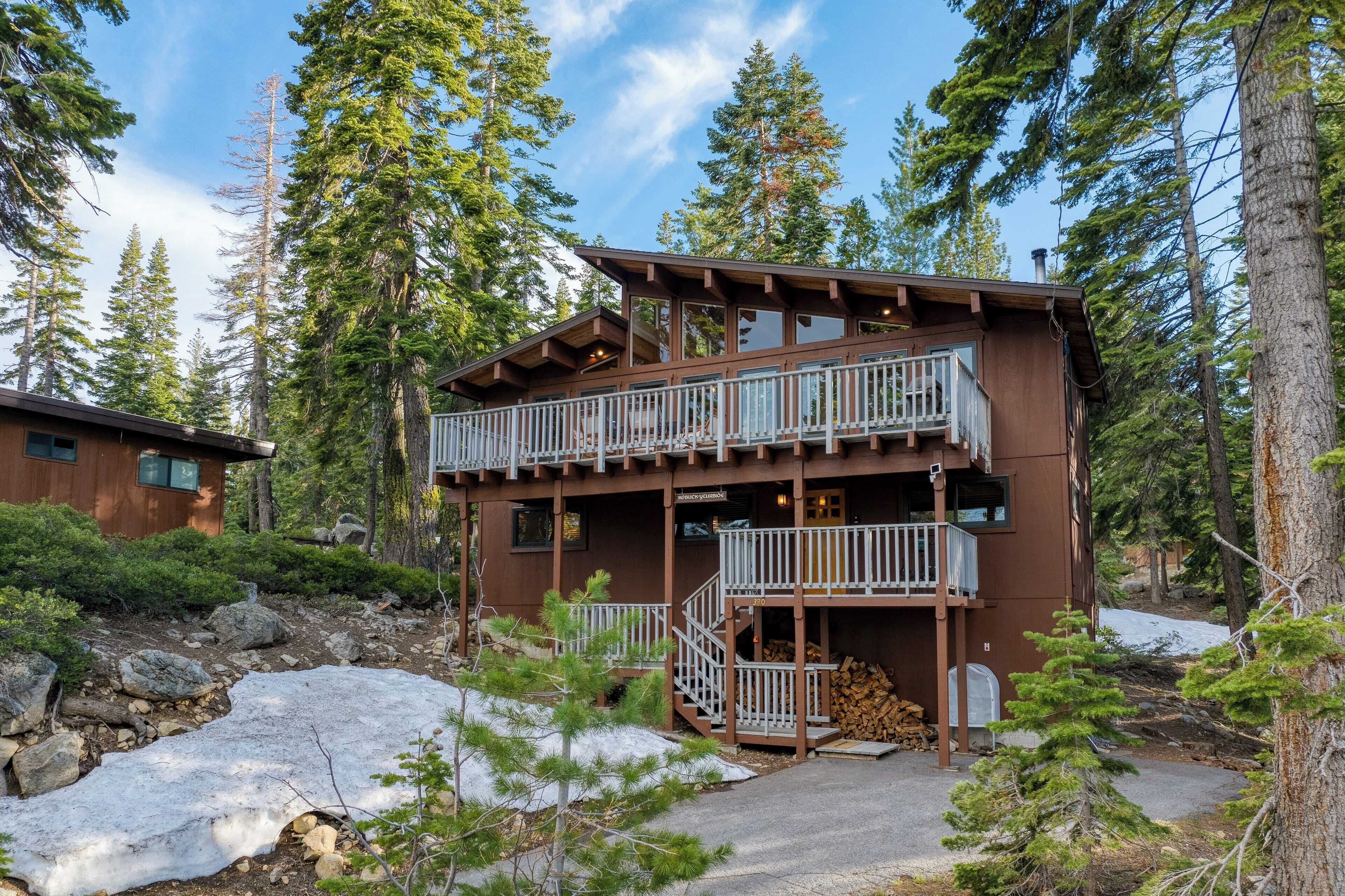 A two-story lodge with a balcony and a fireplace, surrounded by trees and snow.