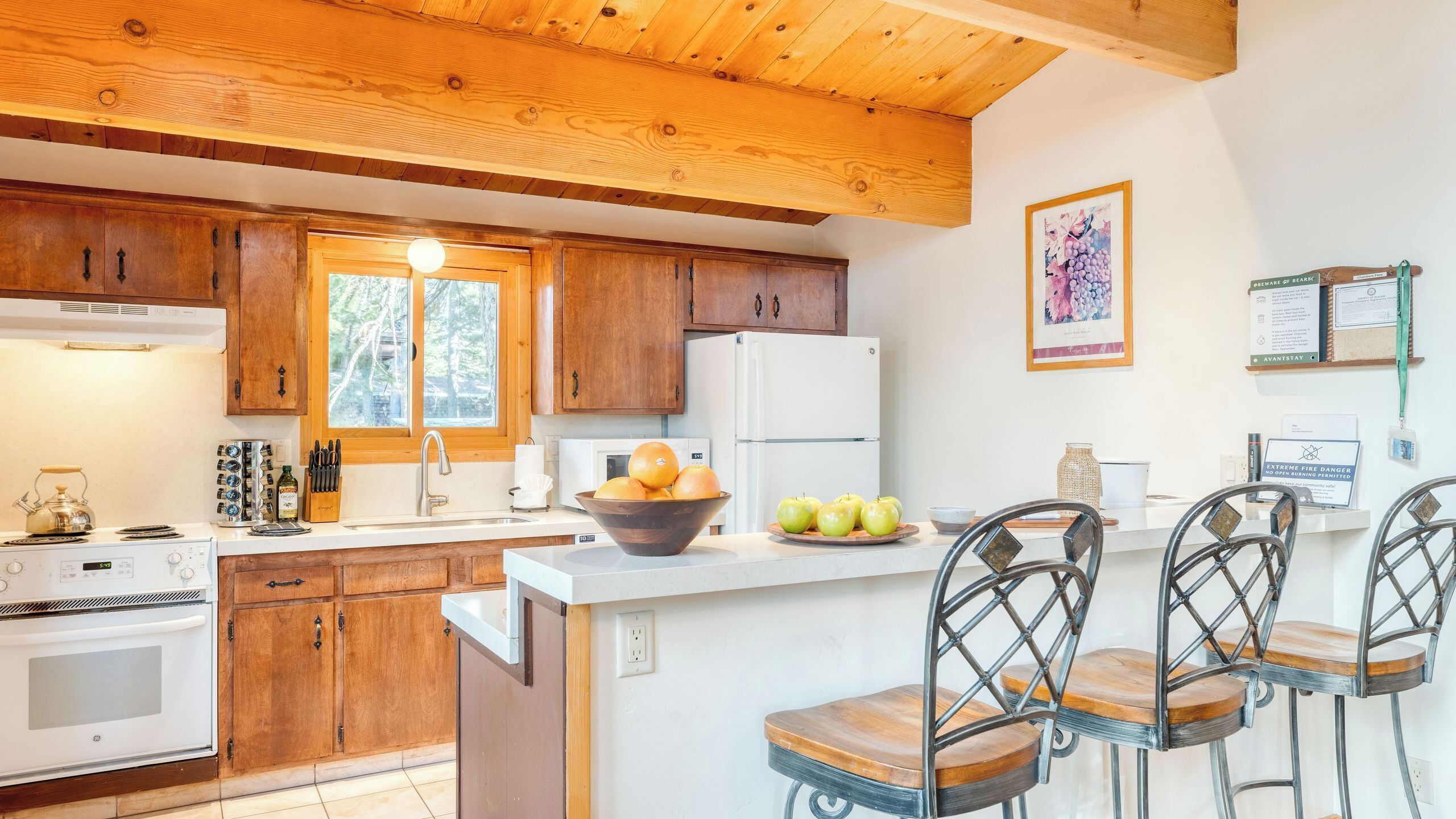 A kitchen with wooden cabinets, a white refrigerator, a sink, and a dining area with metal chairs.