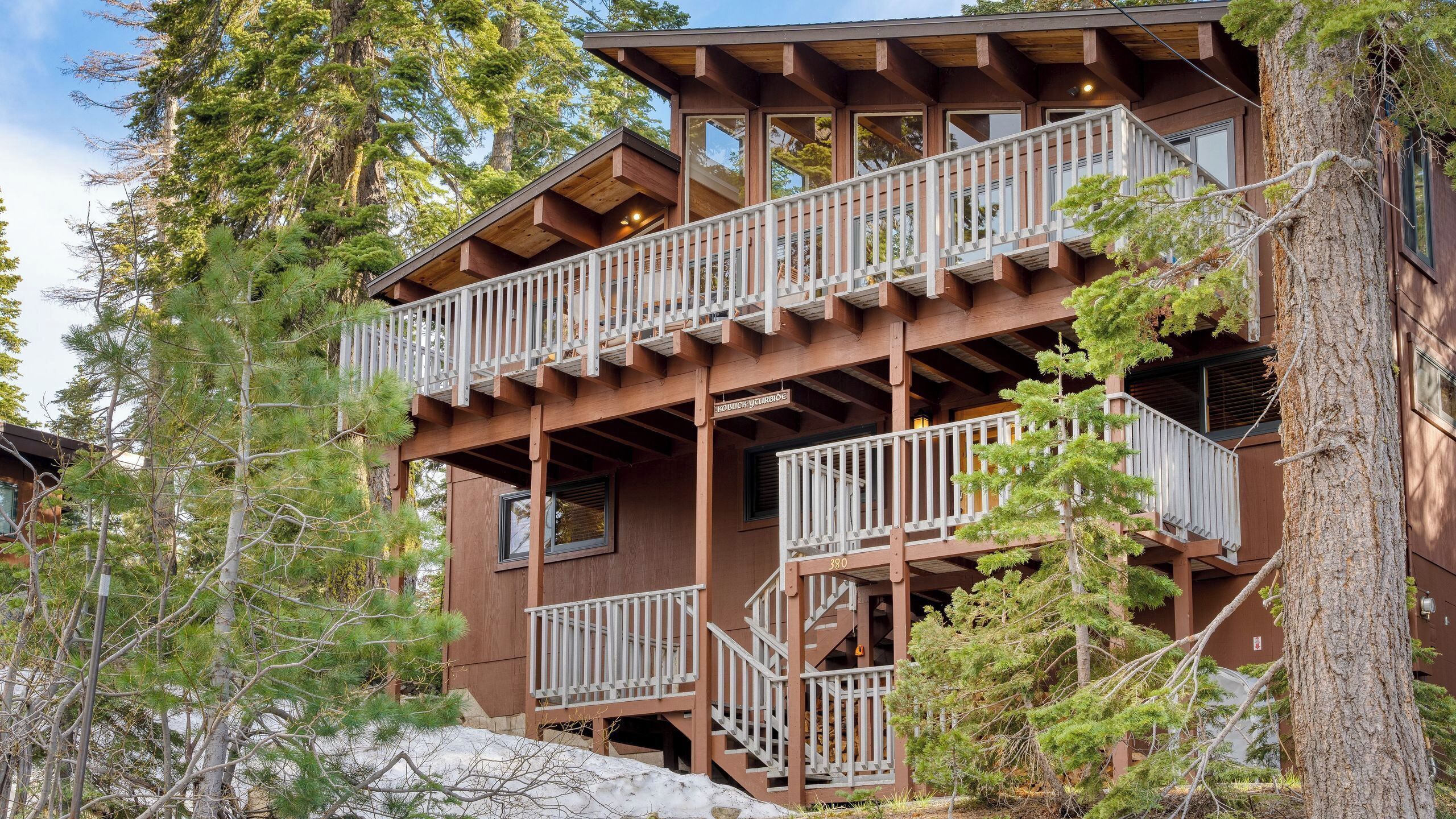 Une cabane en bois à plusieurs étages, dotée de balcons et entourée d’arbres.
