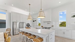 A modern kitchen with white cabinetry, a large island with bar stools, stainless steel appliances, and pendant lighting.