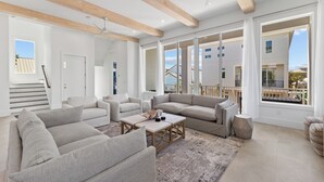 A spacious living room with a high ceiling, built-in wooden beams, large windows, and a view of the outside.