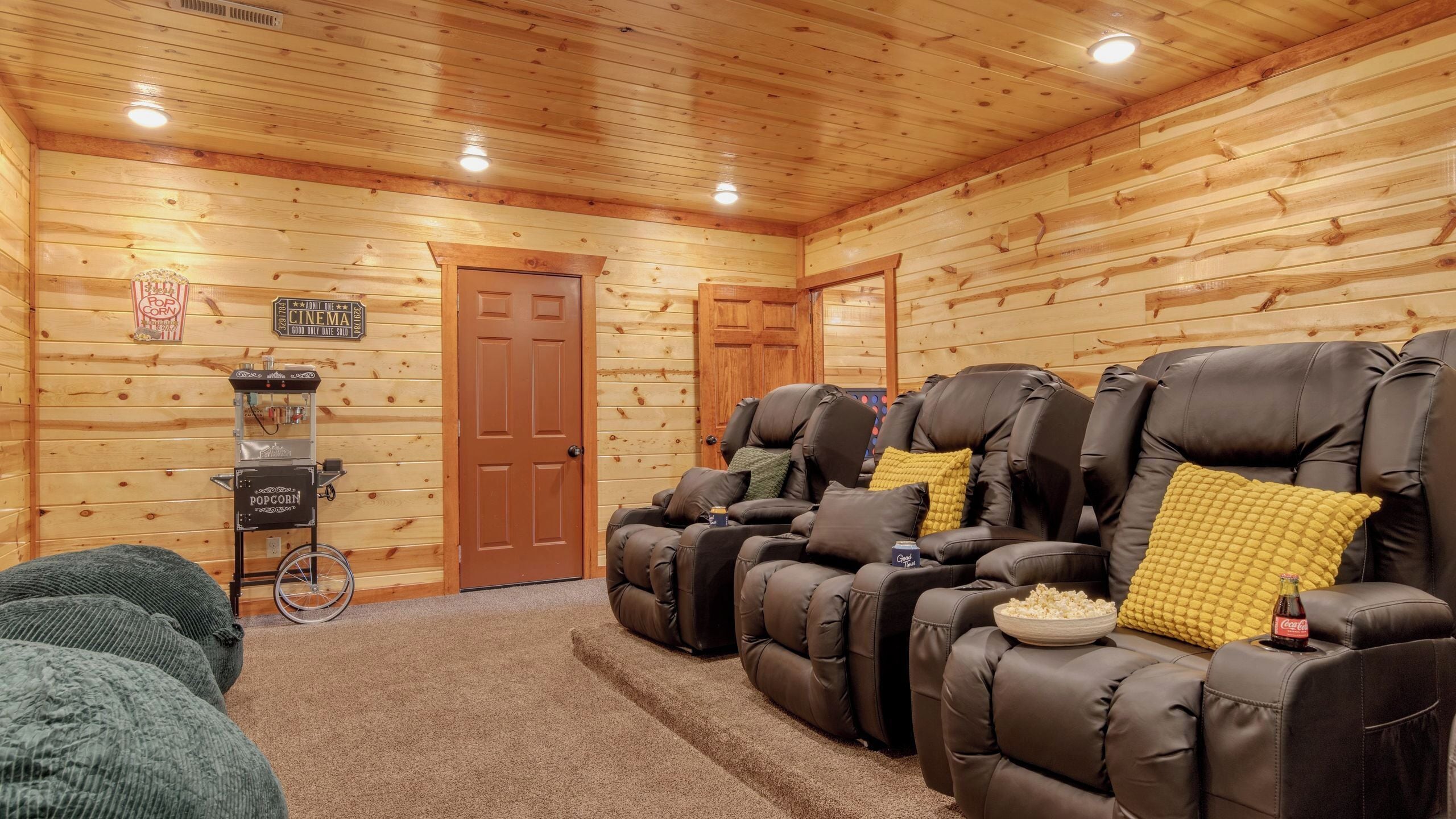 A log cabin interior with a cinema sign, popcorn machine, and reclining chairs.