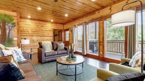 A cozy cabin interior with a wooden ceiling, a sofa, a coffee table, and a view of the outdoors.