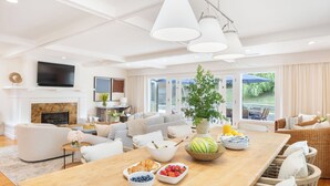 A modern living room with a fireplace, a large dining table with fruit and pastries, a sofa, and a TV mounted on the wall. - La Jolla Living by Avantstay A+ Location Private Backyard Lounge (La Jolla)