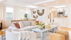 A modern living room with a sofa, ottomans, and a coffee table. There is a kitchen area with a microwave and a sink visible. - La Jolla Living by Avantstay A+ Location Private Backyard Lounge (La Jolla)