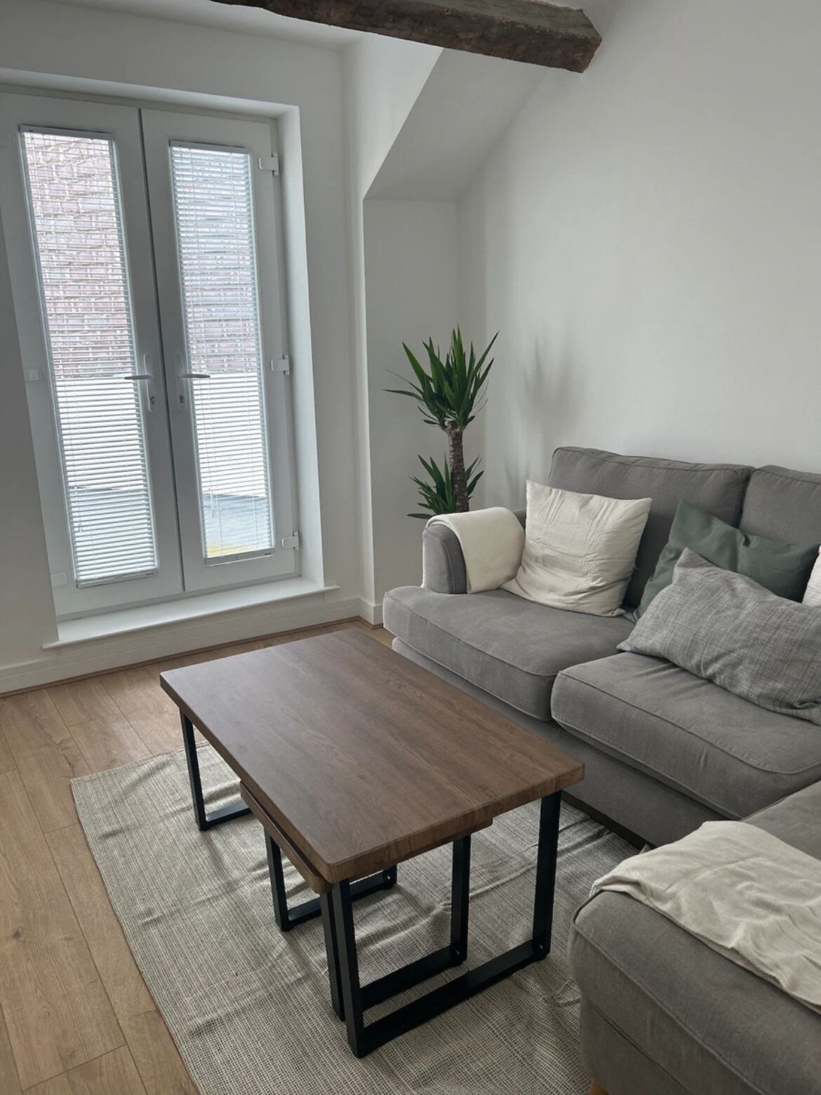Uma sala de estar moderna com um sofá cinzento, uma mesa de centro de madeira e um vaso de planta.