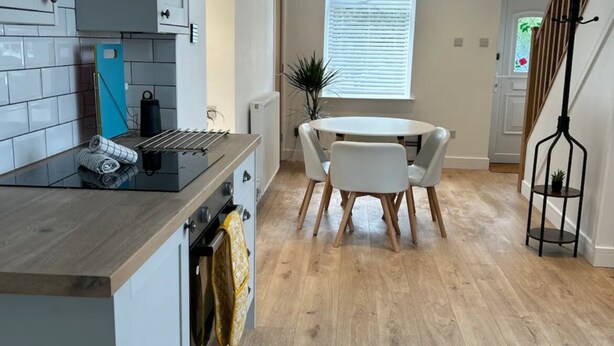 A modern kitchen with white cabinets, a wooden countertop, and a dining area with a white table and chairs. - Bay View House - a countryside retreat close to Snowdon and Zipworld! (Bangor)