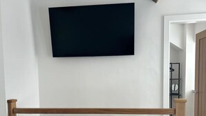 A room with a wooden floor, a black television mounted on the wall, and a wooden railing in the foreground. - Bay View House - a countryside retreat close to Snowdon and Zipworld! (Bangor)