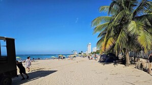 Une plage de sable avec des palmiers, des parasols et une tente.