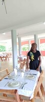 Un área de comedor al aire libre cubierta, con mesas dispuestas para una comida, que incluye manteles blancos y sillas de madera.