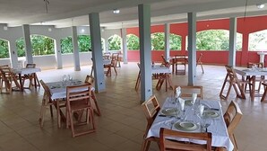 Un vaste espace dédié à la salle à manger, avec de nombreuses tables et chaises, de grandes fenêtres offrant une vue sur la verdure et un mur d’accent de couleur rouge.