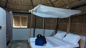 Un lit simple avec une moustiquaire, une tête de lit en bois et un sol en pierre.