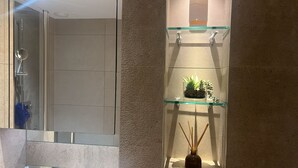 A bathroom with a glass shower enclosure, a glass shelf with a plant, and a reed diffuser. - Impeccable 1-bed Apartment (Barking)
