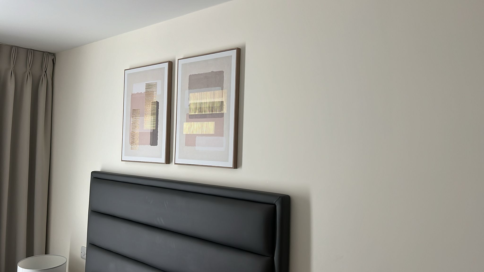 A room with a large, dark headboard and two framed abstract artworks on the wall.